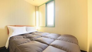 Ein Einzelbett mit Kopfteil, ein Fenster mit grünem Rahmen und eine helle Wand.