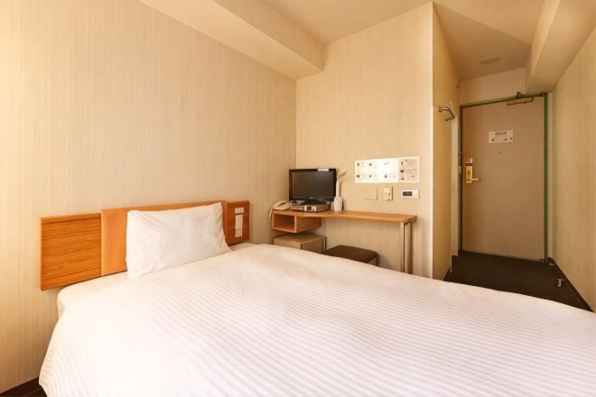A hotel room with a bed, a desk with a computer, and a television.