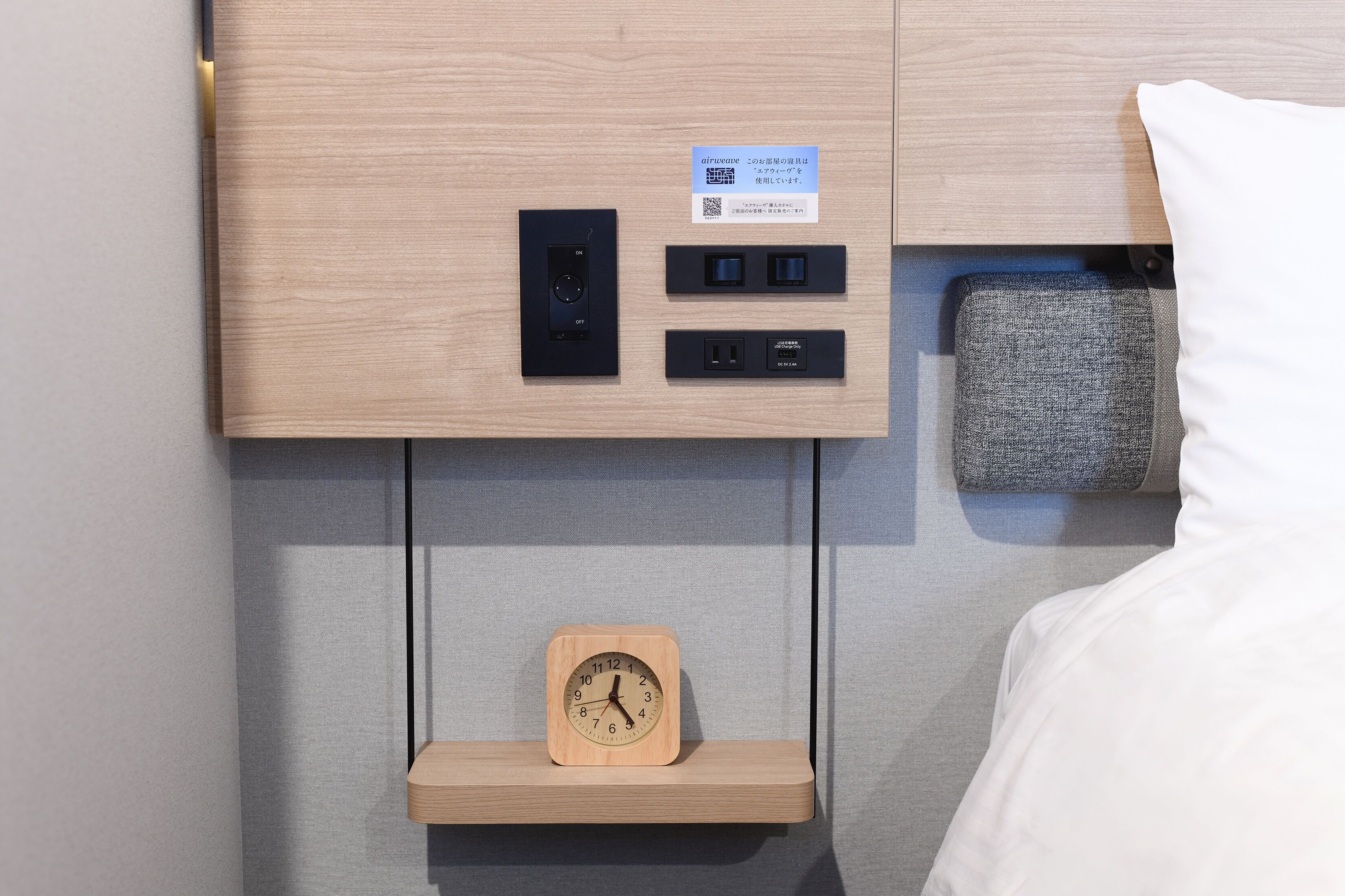 A neatly organized bedroom with a wooden headboard, a bedside table with a clock, and a pillow.