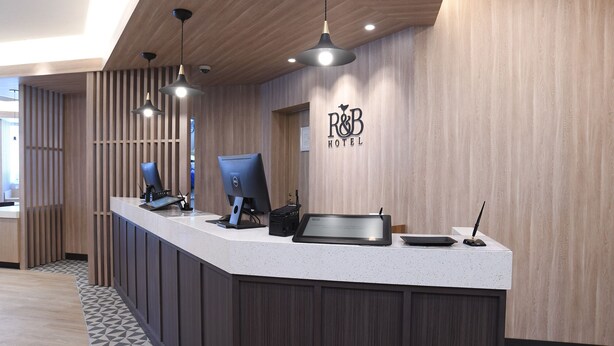 Una recepción de hotel con un panel de pared de madera, un letrero que dice "R&B HOTEL" y dos computadoras Dell.