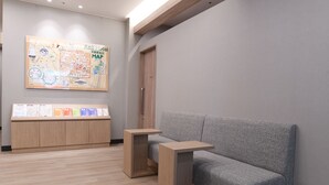 Un lobby moderno de hotel con un mostrador de recepción de madera, un sofá gris y un gran mapa en la pared.
