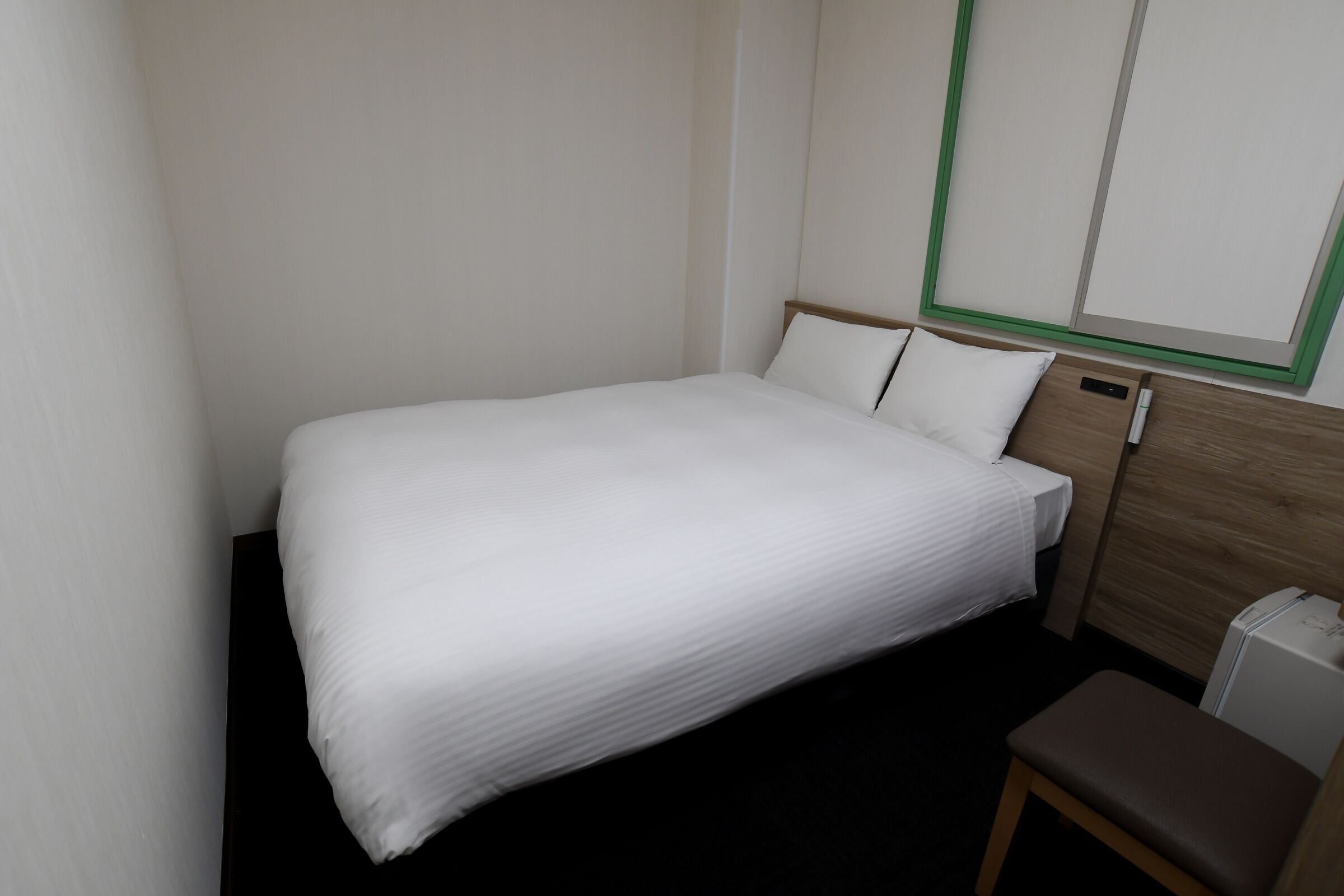 A small, neatly made bed with white bedding in a compact room with a wooden headboard and a small bench.