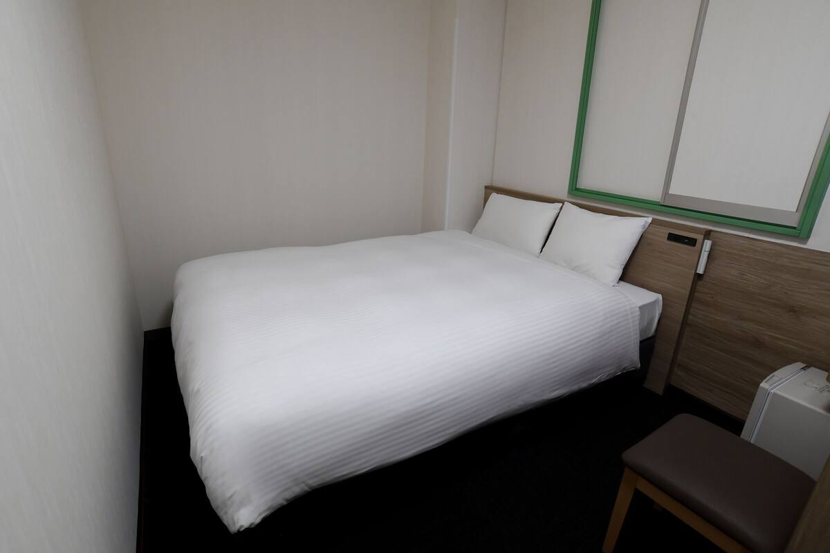 Ein kleines, ordentlich bezogenes Bett mit weißer Bettwäsche in einem kompakten Zimmer, das ein hölzernes Kopfende und eine kleine Bank hat.