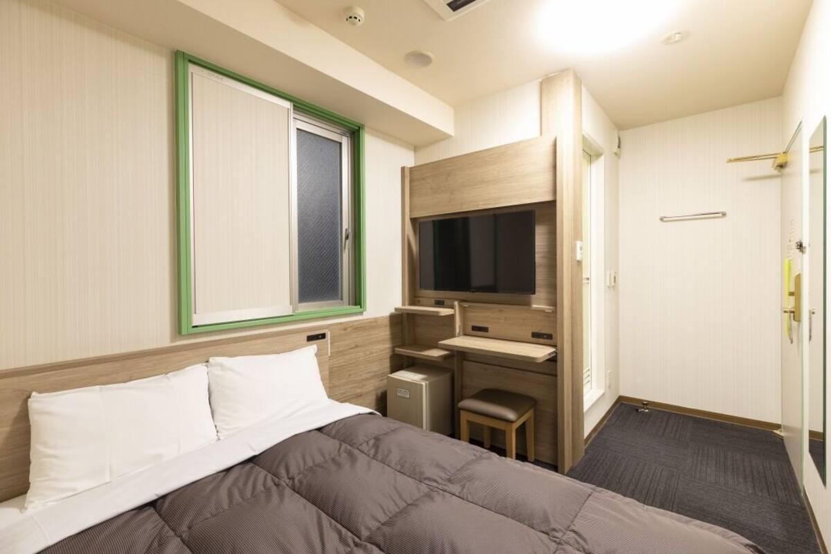 Ein Hotelzimmer mit Bett, Schreibtisch, Fernseher und einem kleinen Schrank.