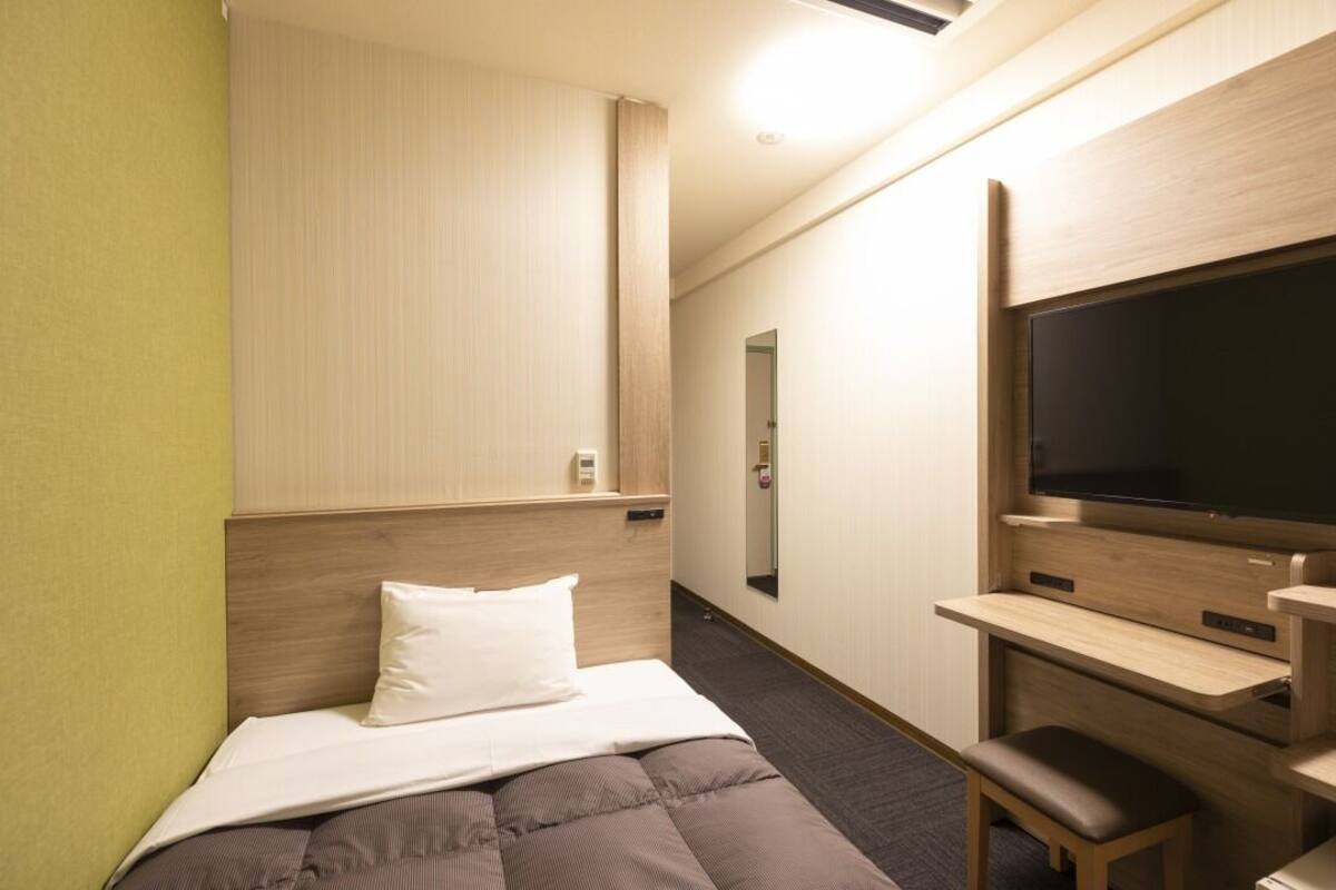 Ein Hotelzimmer mit Bett, Schreibtisch, Stuhl, Fernseher und Spiegel.