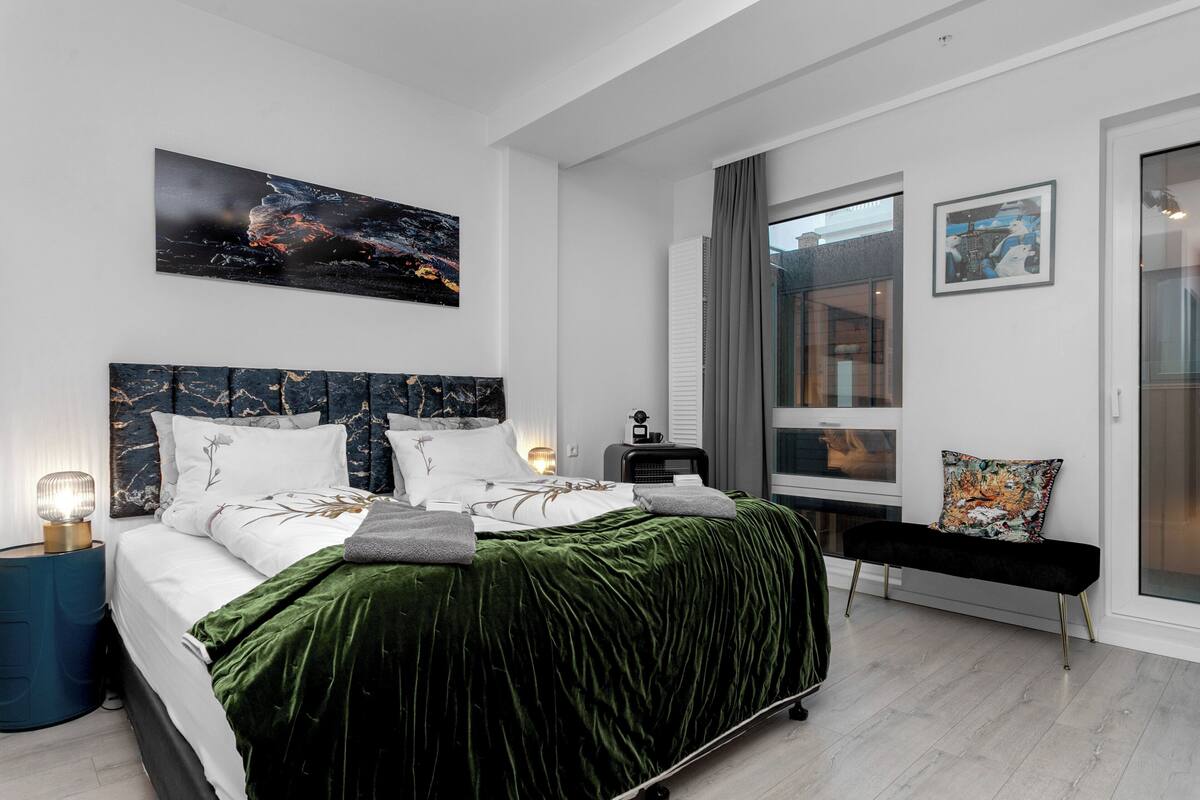 A modern bedroom with a large bed, a side table, a bench, and artwork on the walls.