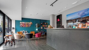 Un espace d’accueil moderne avec un mur de couleur turquoise, un grand tableau et divers types de sièges, notamment un fauteuil rose et une table en bois.