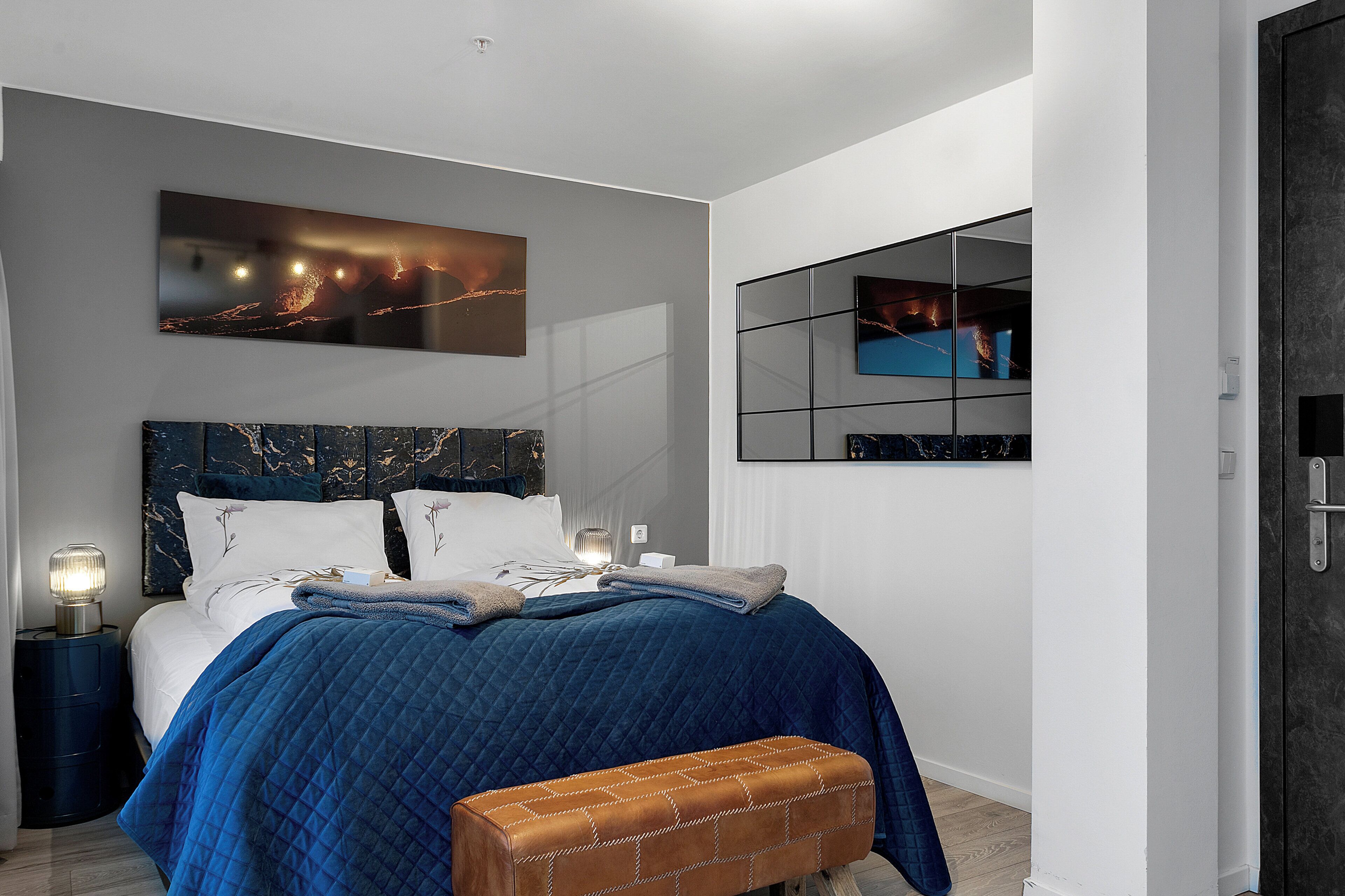 Un dormitorio moderno con una cama grande, un banco, una mesita de noche y un televisor instalado en la pared.