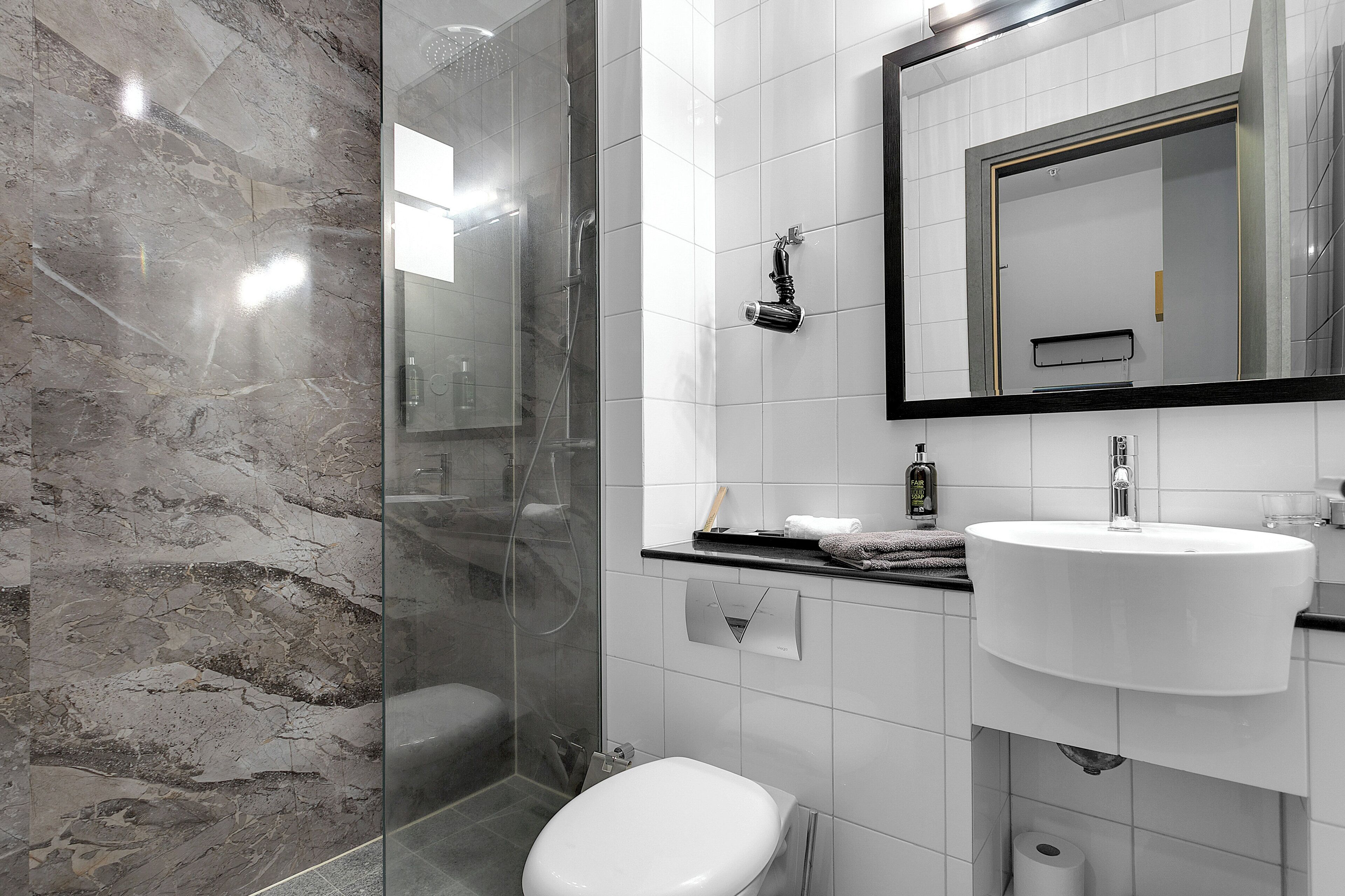 Un baño moderno con ducha de vidrio, lavamanos blanco y pared de azulejos de mármol.
