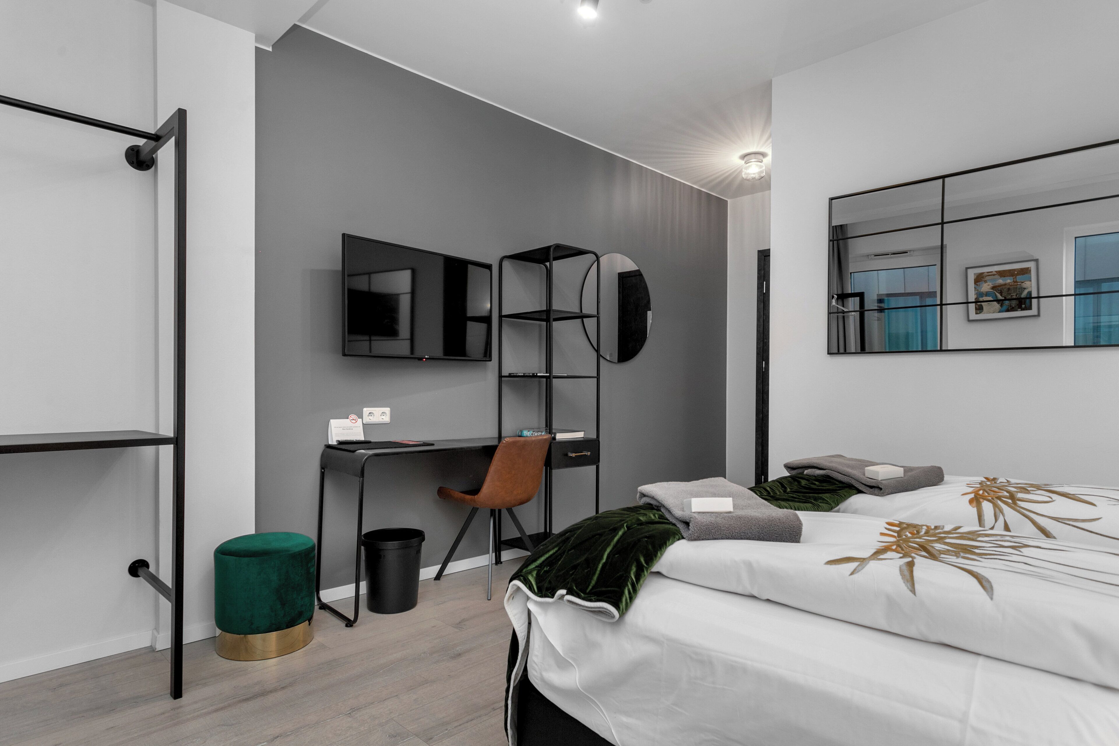 A modern bedroom with a bed, a desk, a chair, and a large mirror.