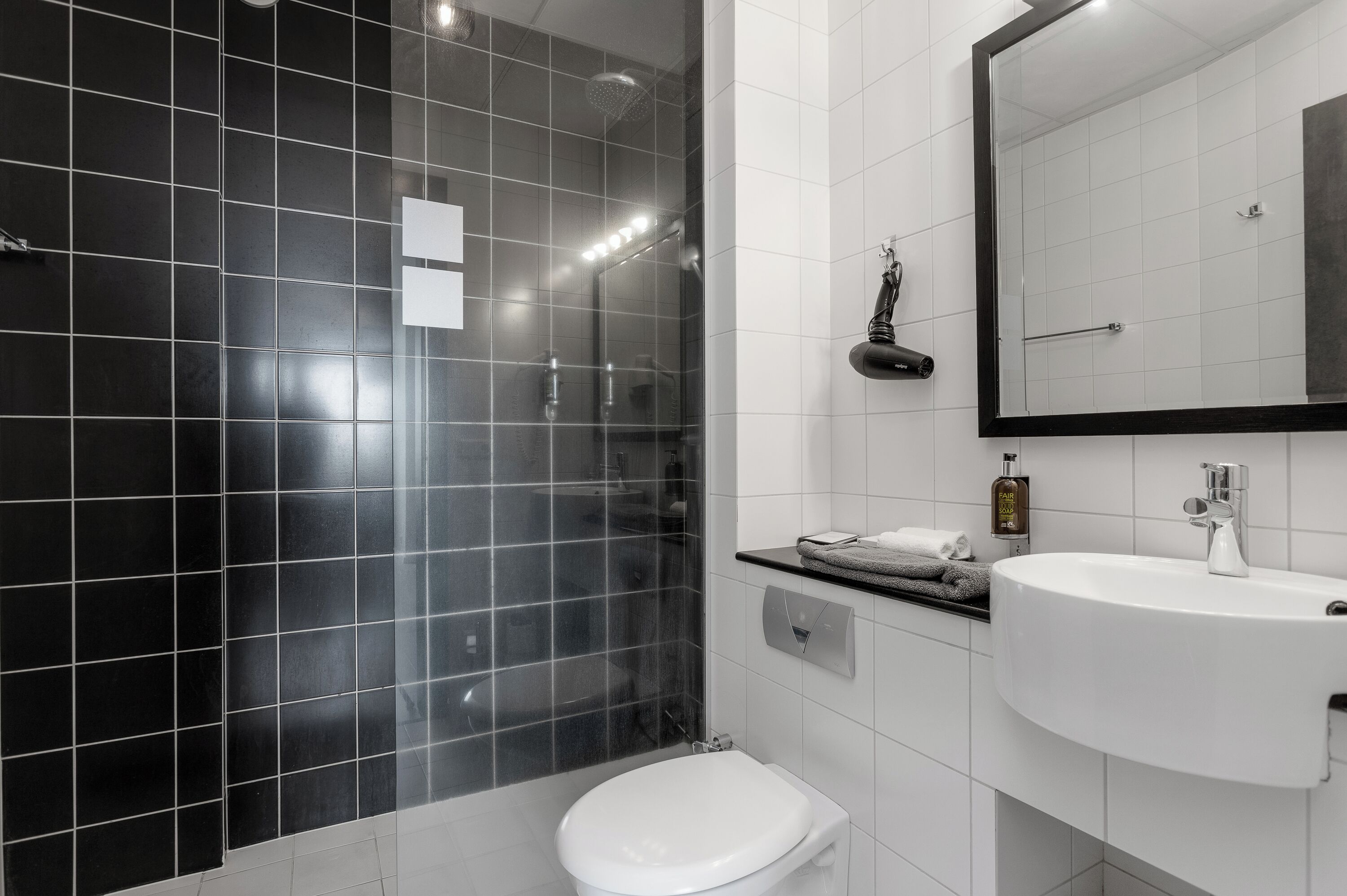 A modern bathroom with black and white tiles, a white sink, and a glass-enclosed shower.