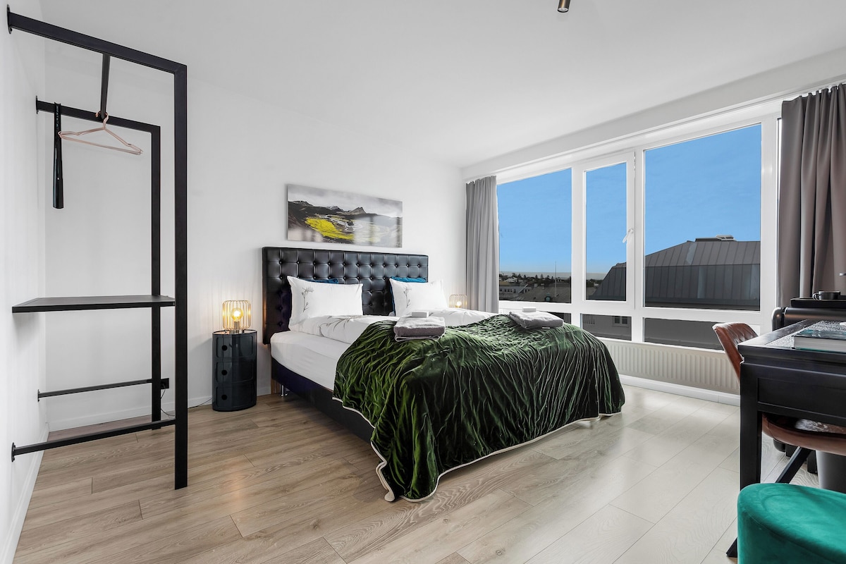 Une chambre moderne avec un lit, un bureau et une grande fenêtre donnant sur la ville.