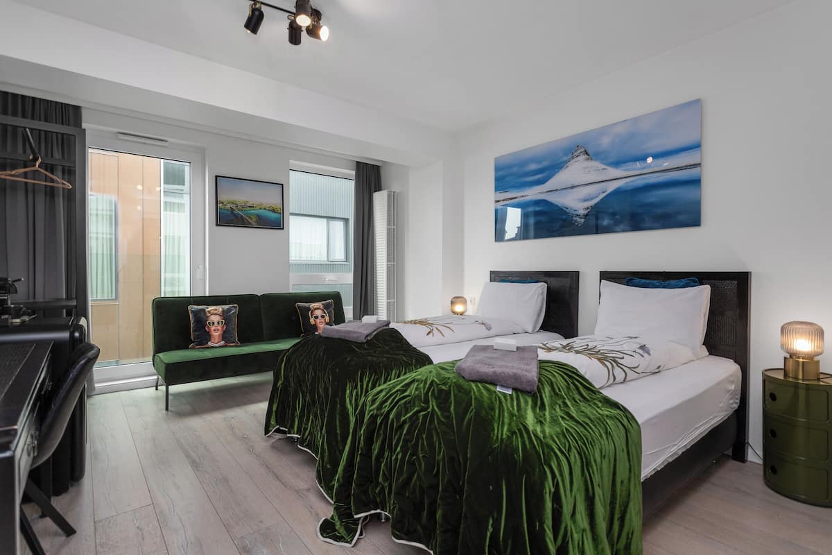 A modern hotel room with a bed, a desk, and a green sofa.
