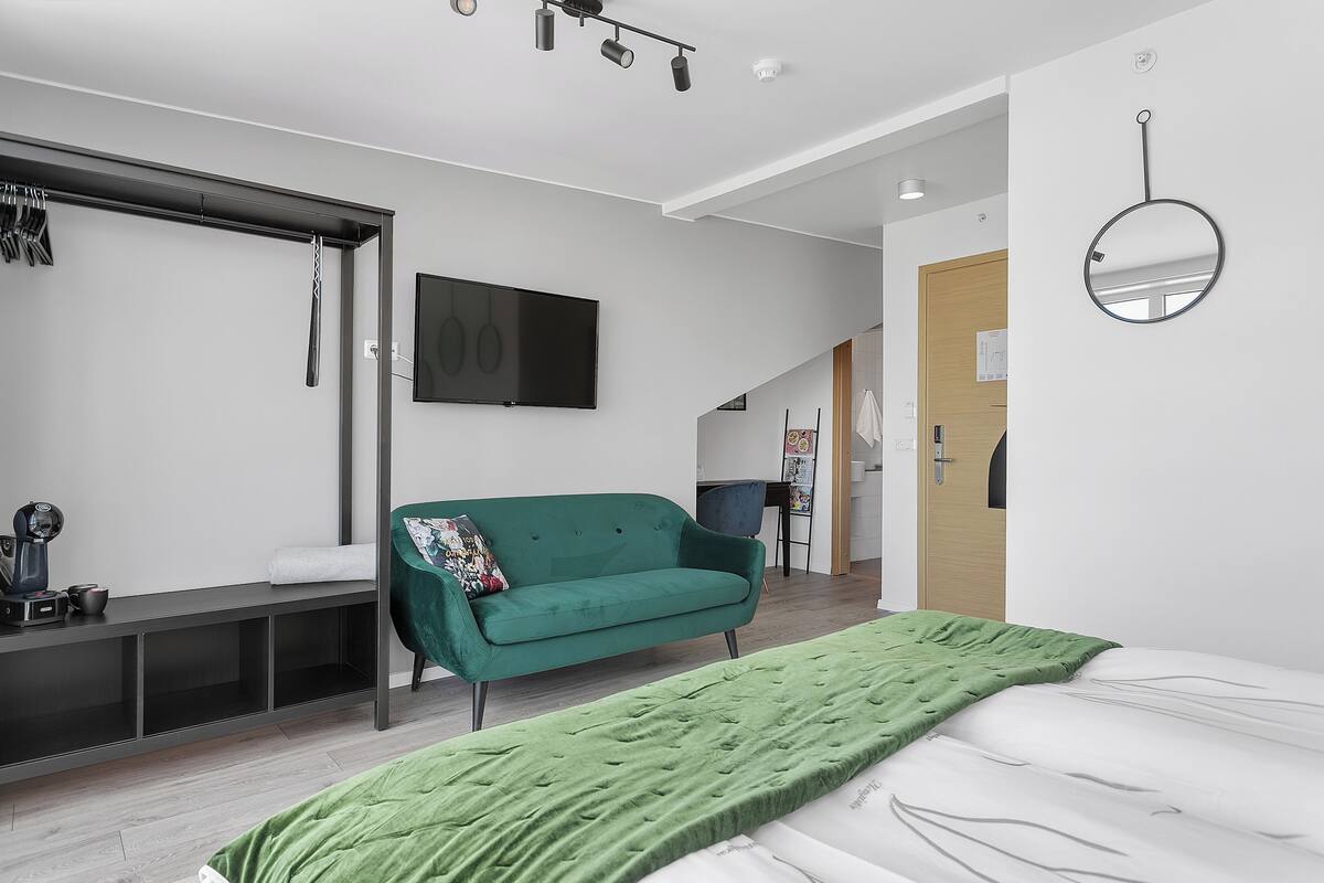 A modern bedroom with a bed, a green sofa, a TV, and a mirror.
