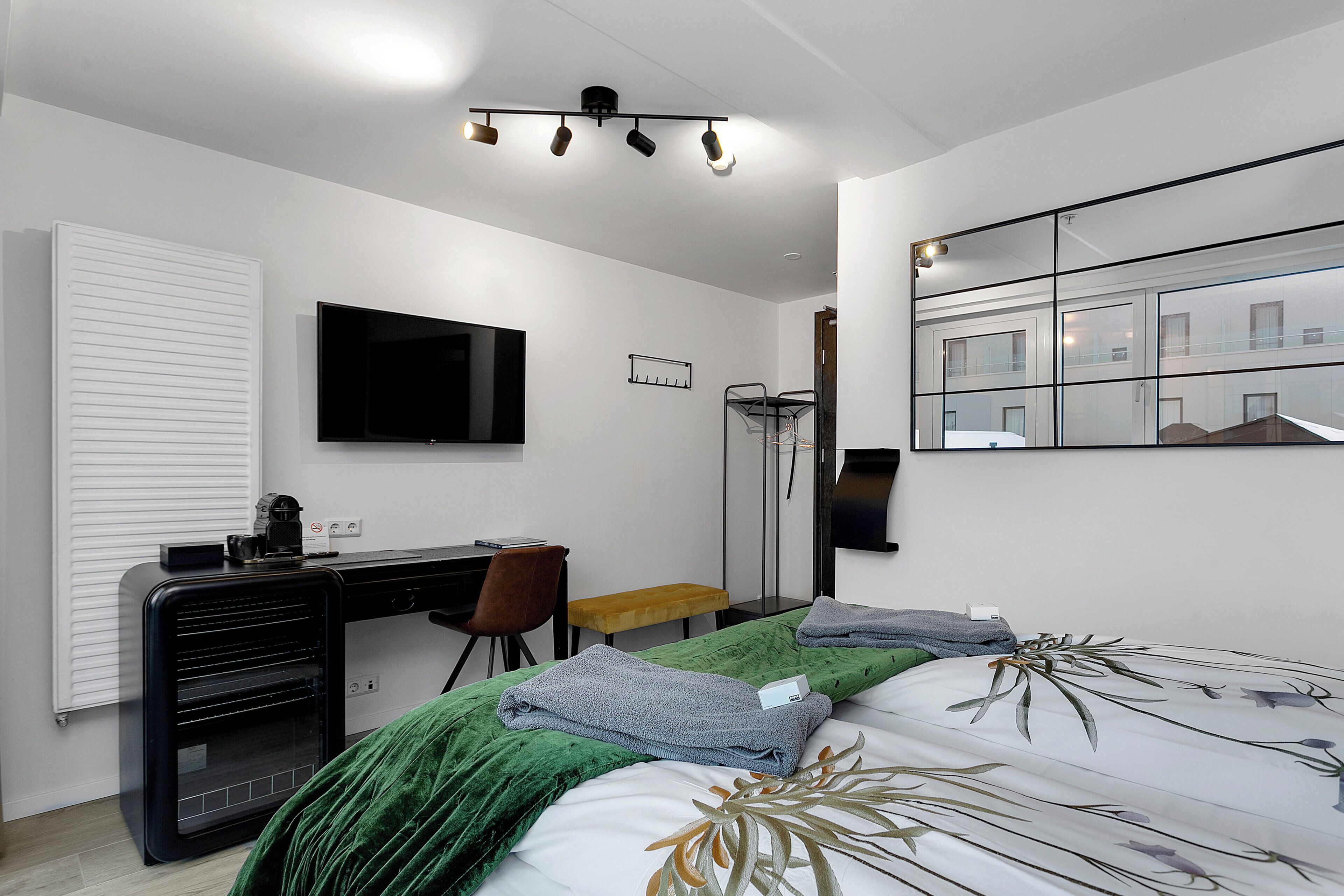 Een moderne hotelkamer met een bed, bureau, stoel, televisie en spiegel.