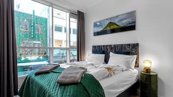 Une chambre d’hôtel avec un grand lit, une table de chevet avec une lampe, un tableau au mur et une vue sur un bâtiment à l’extérieur.