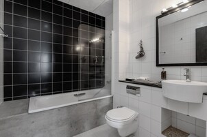 A modern bathroom with a black tiled shower, a white toilet, and a white sink with a mirror above it.
