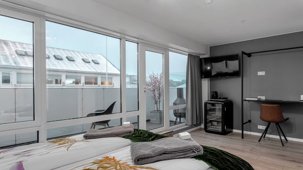 Une chambre d’hôtel moderne dotée d’un grand lit, d’un bureau, d’une télévision et offrant une vue sur le paysage urbain grâce à de grandes fenêtres.
