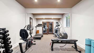 Un gimnasio con cintas de correr, elípticas, banca y mancuernas.