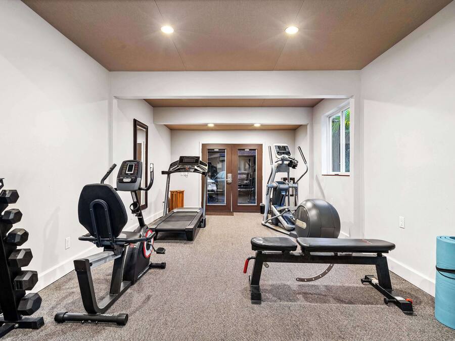 Un gimnasio con cintas de correr, elípticas, banca y mancuernas.