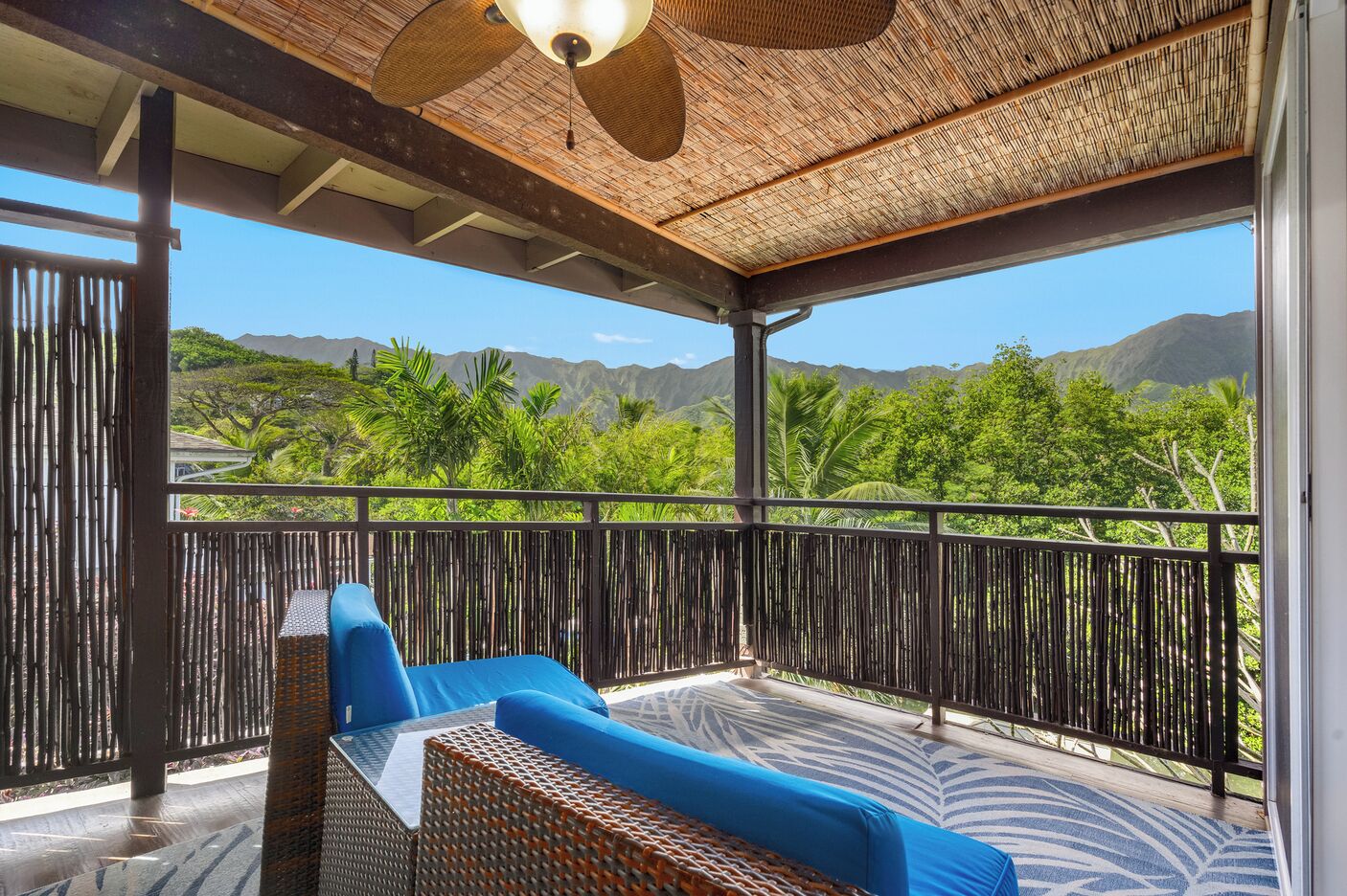 A covered outdoor seating area with wicker furniture and a view of a mountainous landscape.