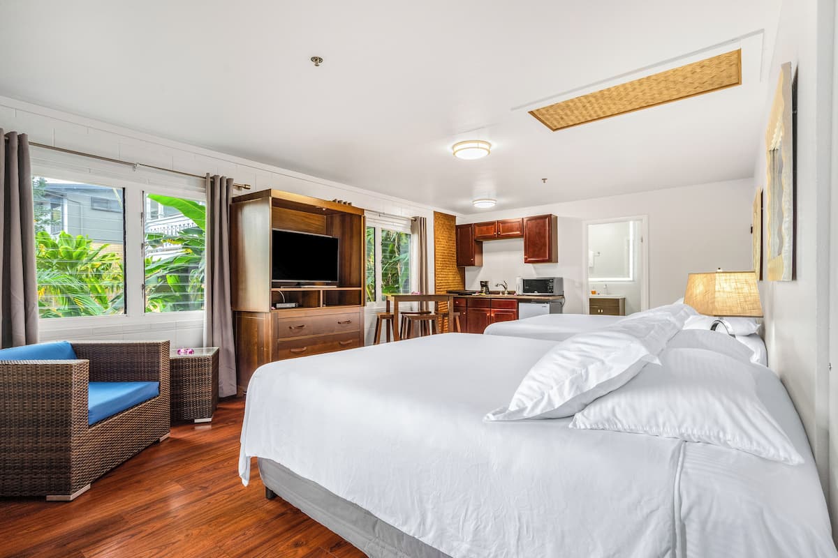 A hotel room with a large bed, a sofa, a desk, and a kitchen area.