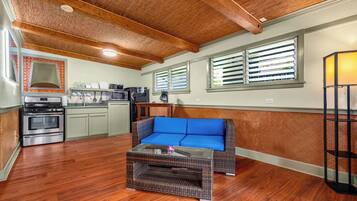 A compact kitchen with a built-in oven, microwave, and coffee maker. A blue cushioned bench is positioned in the center, and a wicker coffee table is in front of it.