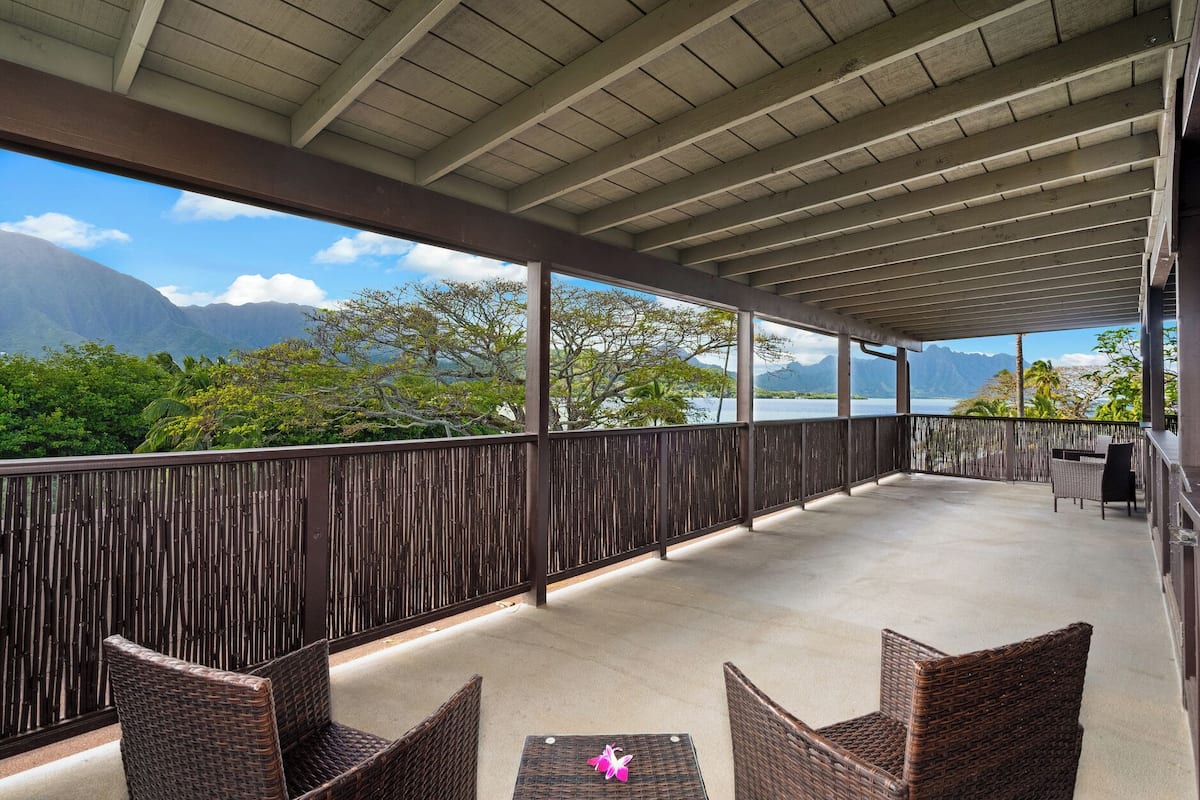 A covered outdoor area with wicker furniture and a view of mountains and trees.