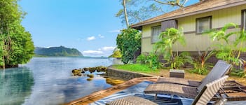 A serene waterfront property with a wooden deck, lounge chairs, and lush greenery.