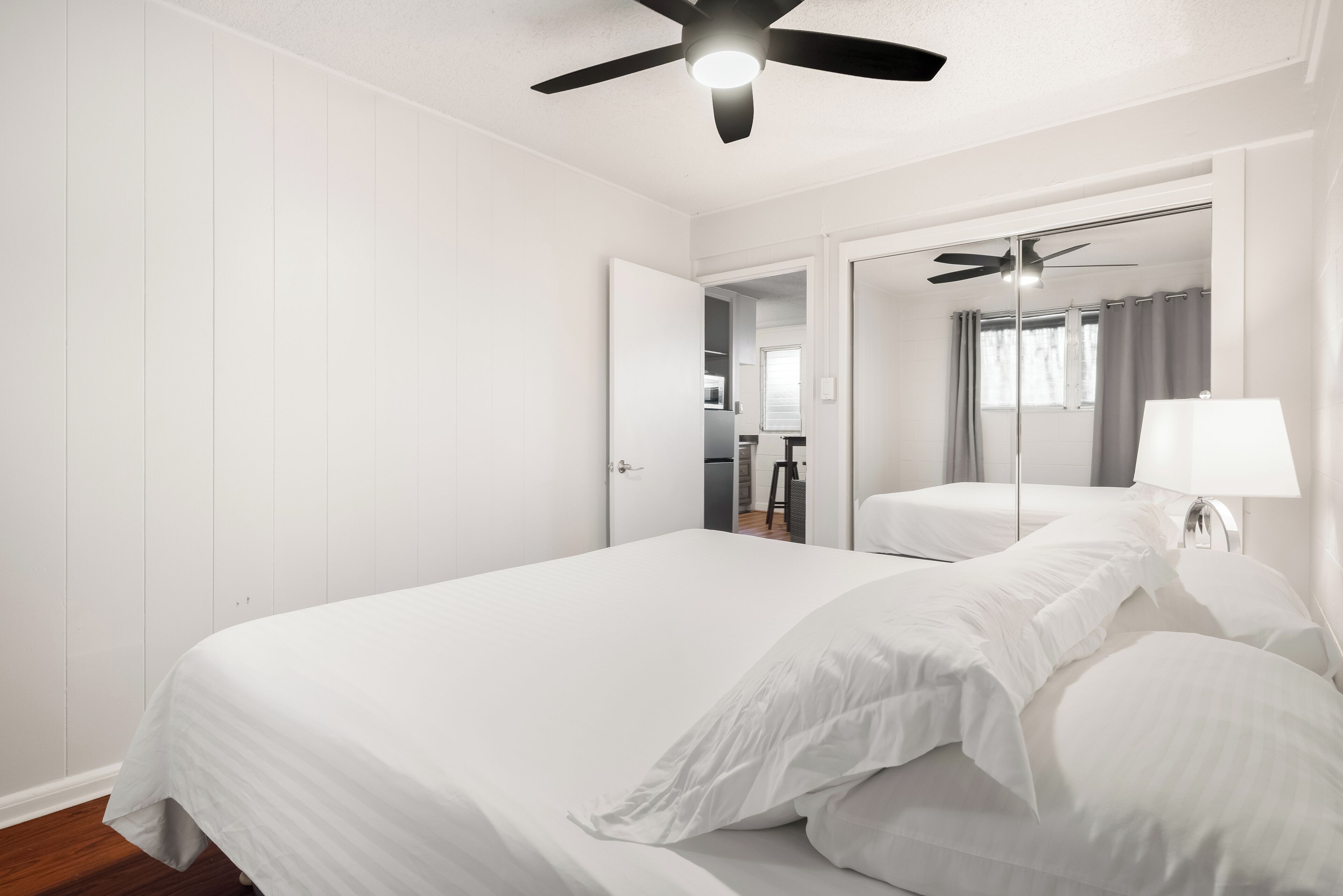 A bedroom with a large bed, a ceiling fan, a mirror, and a lamp.