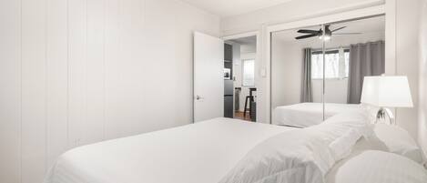 A bedroom with a large bed, a ceiling fan, a mirror, and a lamp.