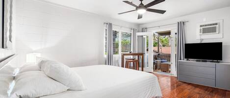 A bedroom with a bed, a ceiling fan, a TV, and a balcony with outdoor furniture.