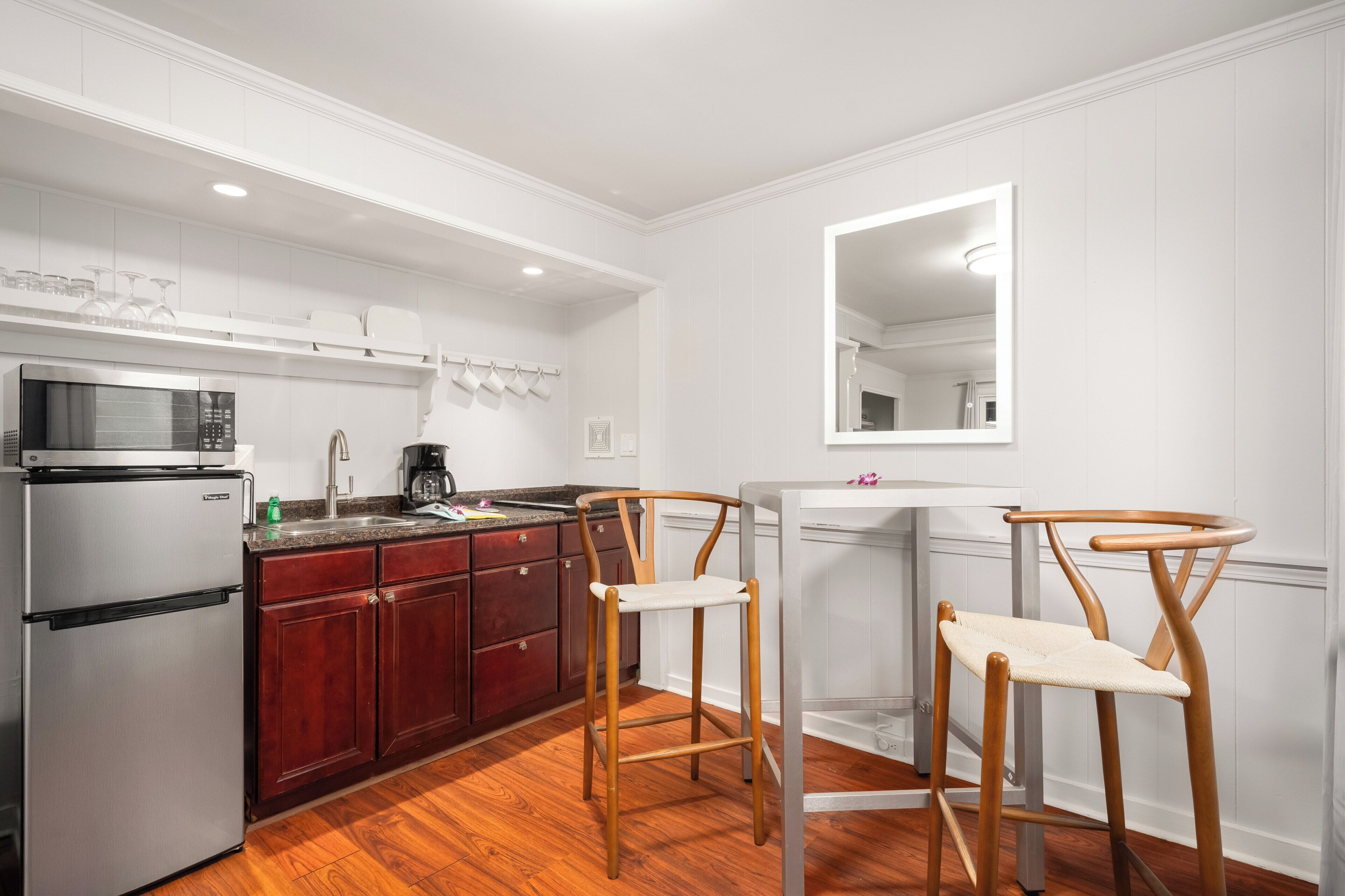 A kitchen with white cabinets, a stainless steel refrigerator, a microwave, a coffee maker, and two wooden chairs.