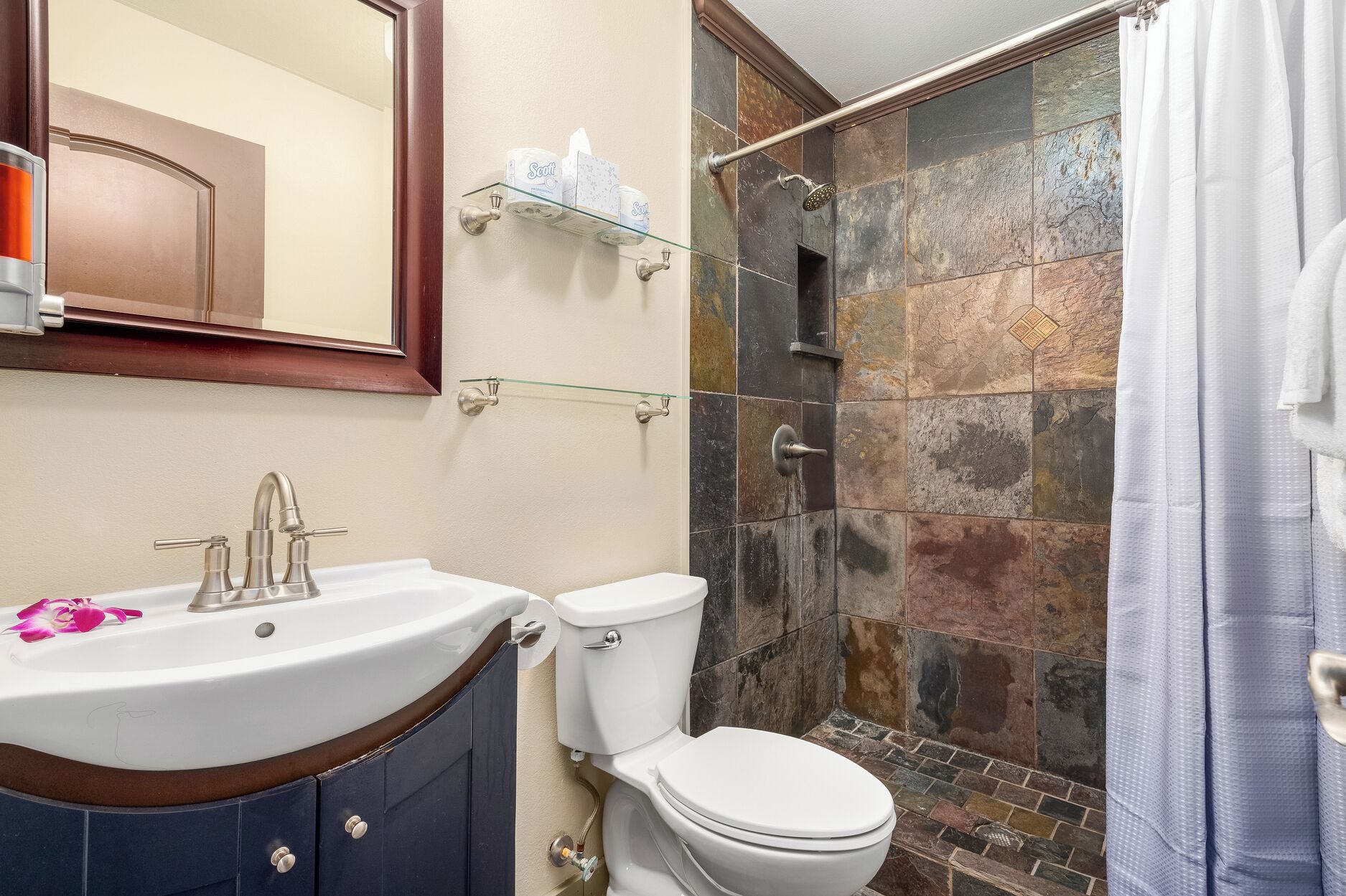 Une salle de bain avec un lavabo blanc, des toilettes et un espace douche carrelé de pierres.