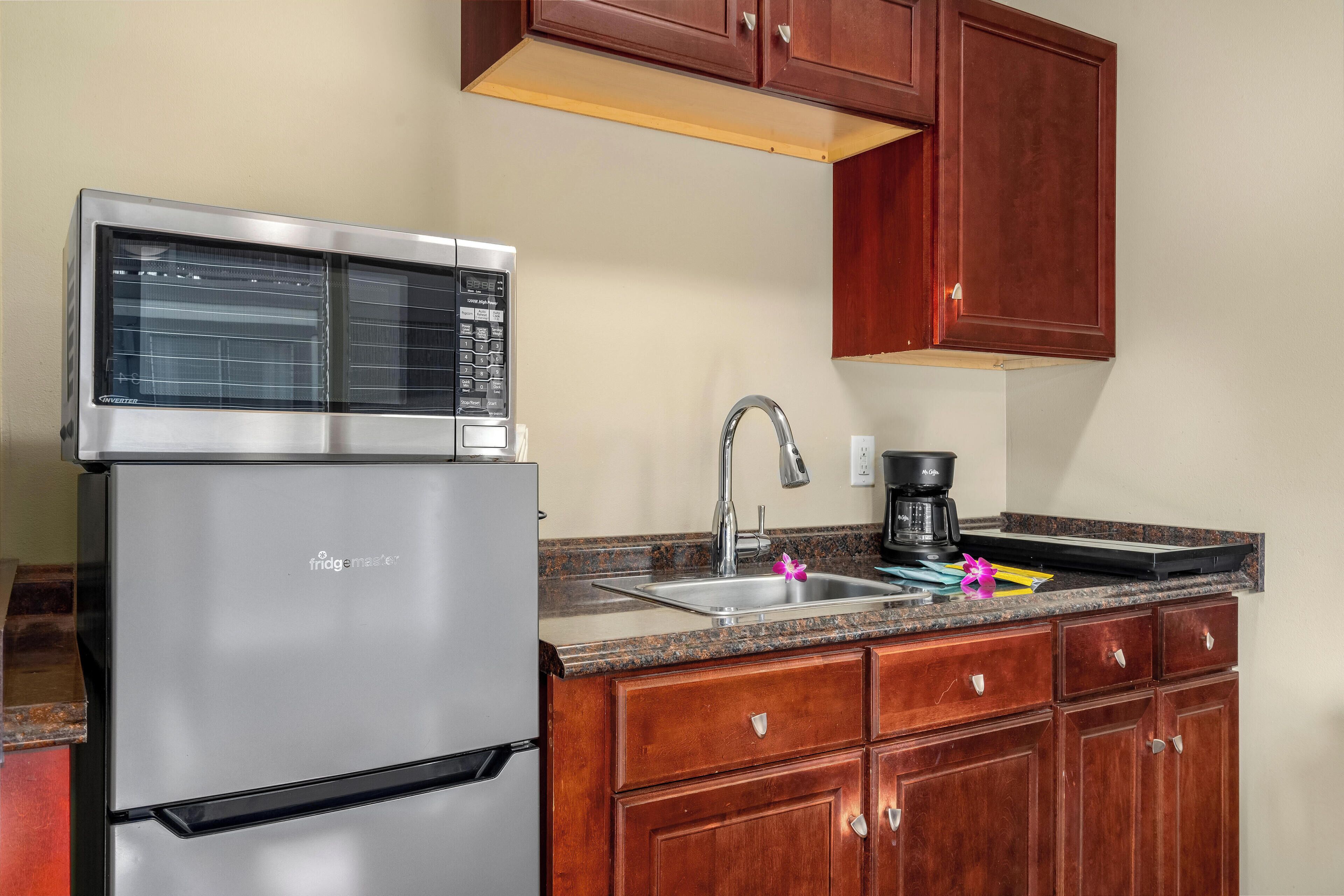 Una cocina con refrigerador de acero inoxidable, encimera de granito, pileta y muebles de madera.
