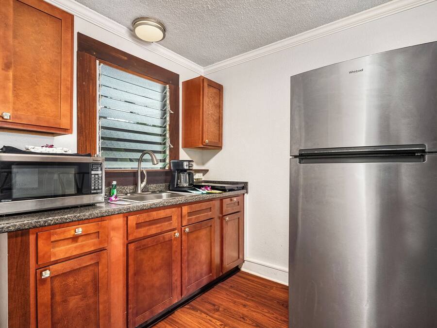 A kitchen with wooden cabinets, a stainless steel refrigerator, a microwave, and a window with blinds.