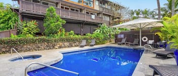 A swimming pool with a stone border, lounge chairs, and a covered seating area with umbrellas.