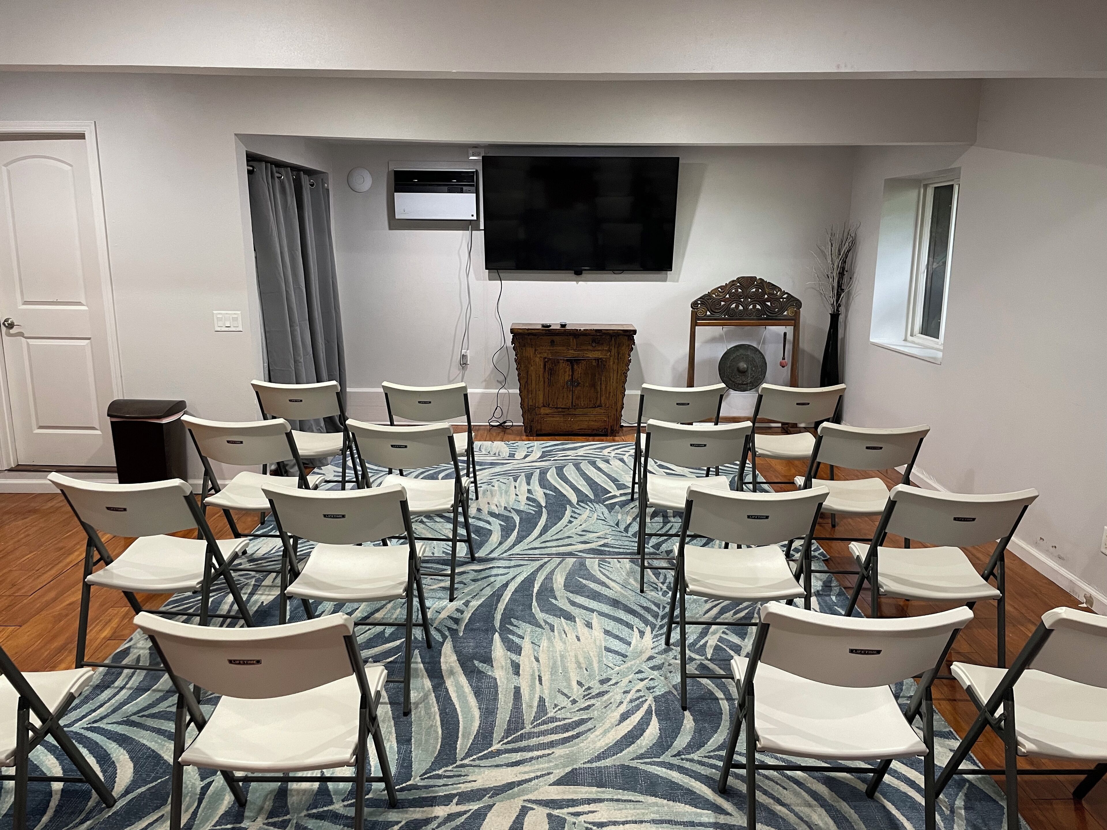 A conference room with rows of white chairs, a large flat-screen TV, a wooden cabinet, and a patterned carpet.