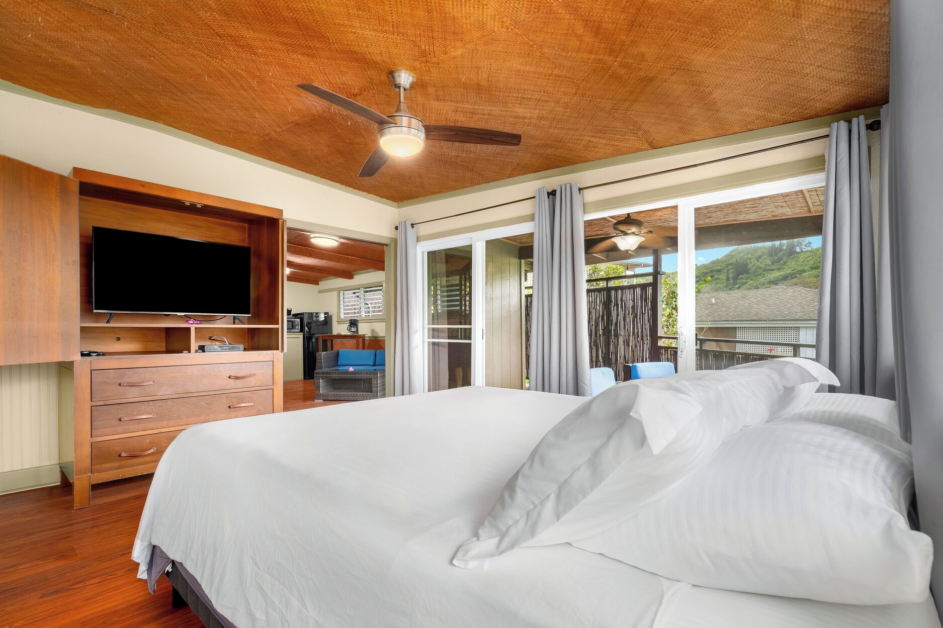 A bedroom with a bed, wooden ceiling, ceiling fan, and a view of the outdoors.