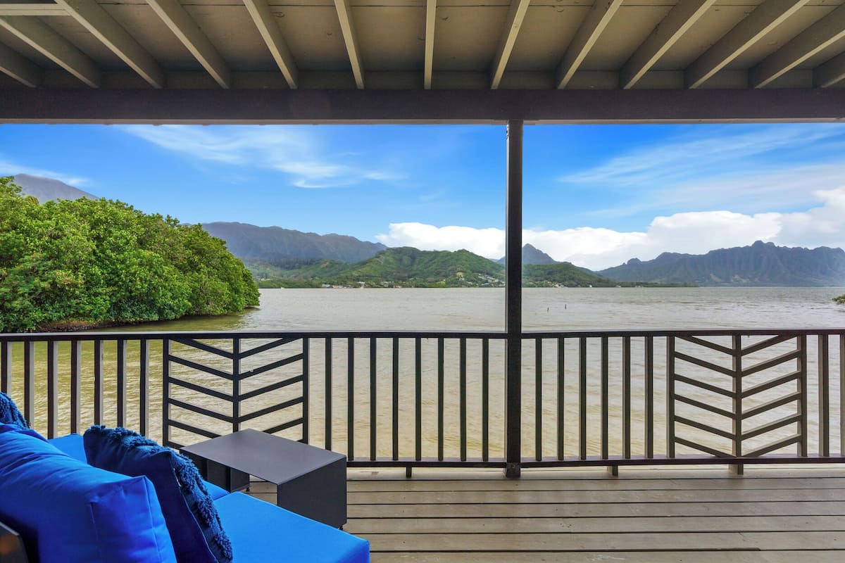 A covered deck with a view of a lake and mountains.