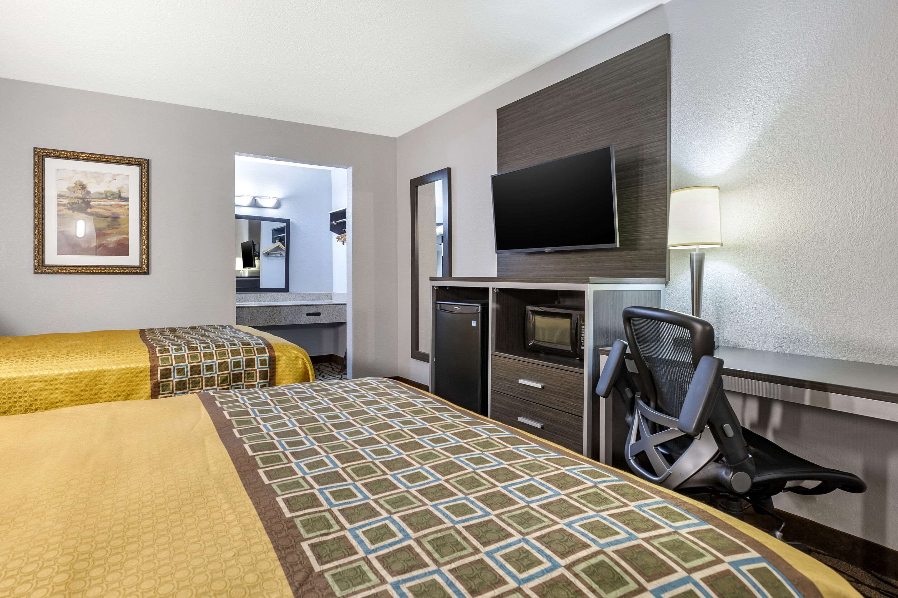 A hotel room with two beds, a desk with a computer, a TV, and a chair.