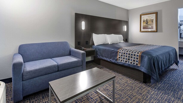Una habitación de hotel con cama, sofá, mesita de noche y una pequeña mesa.