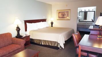 Una habitación de hotel con cama, escritorio, silla, sofá, lámpara, un cuadro y espejo.