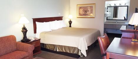 Una habitación de hotel con cama, escritorio, silla, sofá, lámpara, un cuadro y espejo.