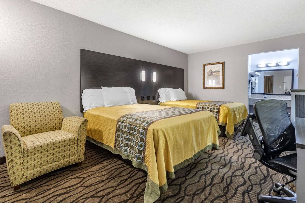 A hotel room with two beds, a chair, a desk, and a mirror.