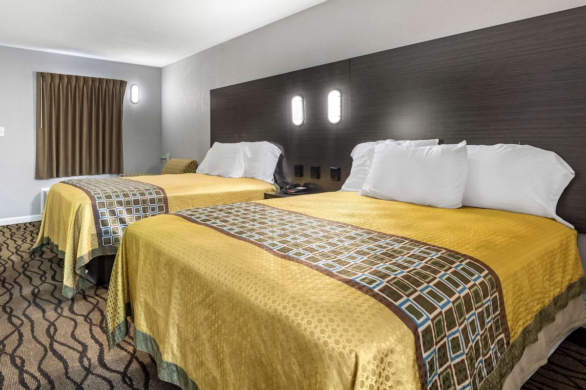 A hotel room with two beds, each with a patterned bedspread and pillows, a dark headboard, and a window with curtains.