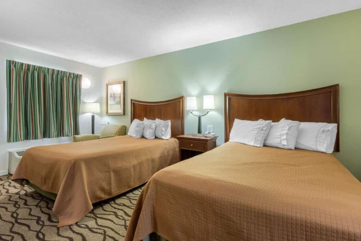 A hotel room with two beds, a nightstand, a lamp, a framed picture, and a window with curtains.
