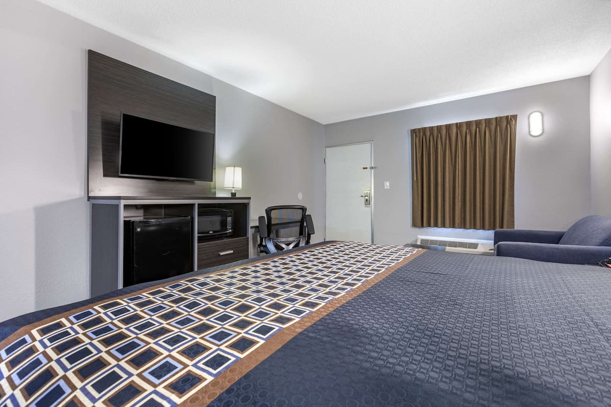 A hotel room with a large bed, a TV mounted on the wall, a desk with a chair, and a window with curtains.