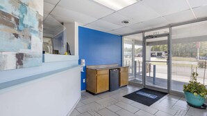 Un área de recepción con pared azul, mostrador de madera, puerta de vidrio que da al exterior y una planta en maceta.