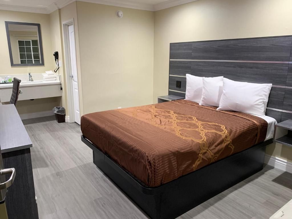 A hotel room with a bed, a desk, a chair, a mirror, and a nightstand.